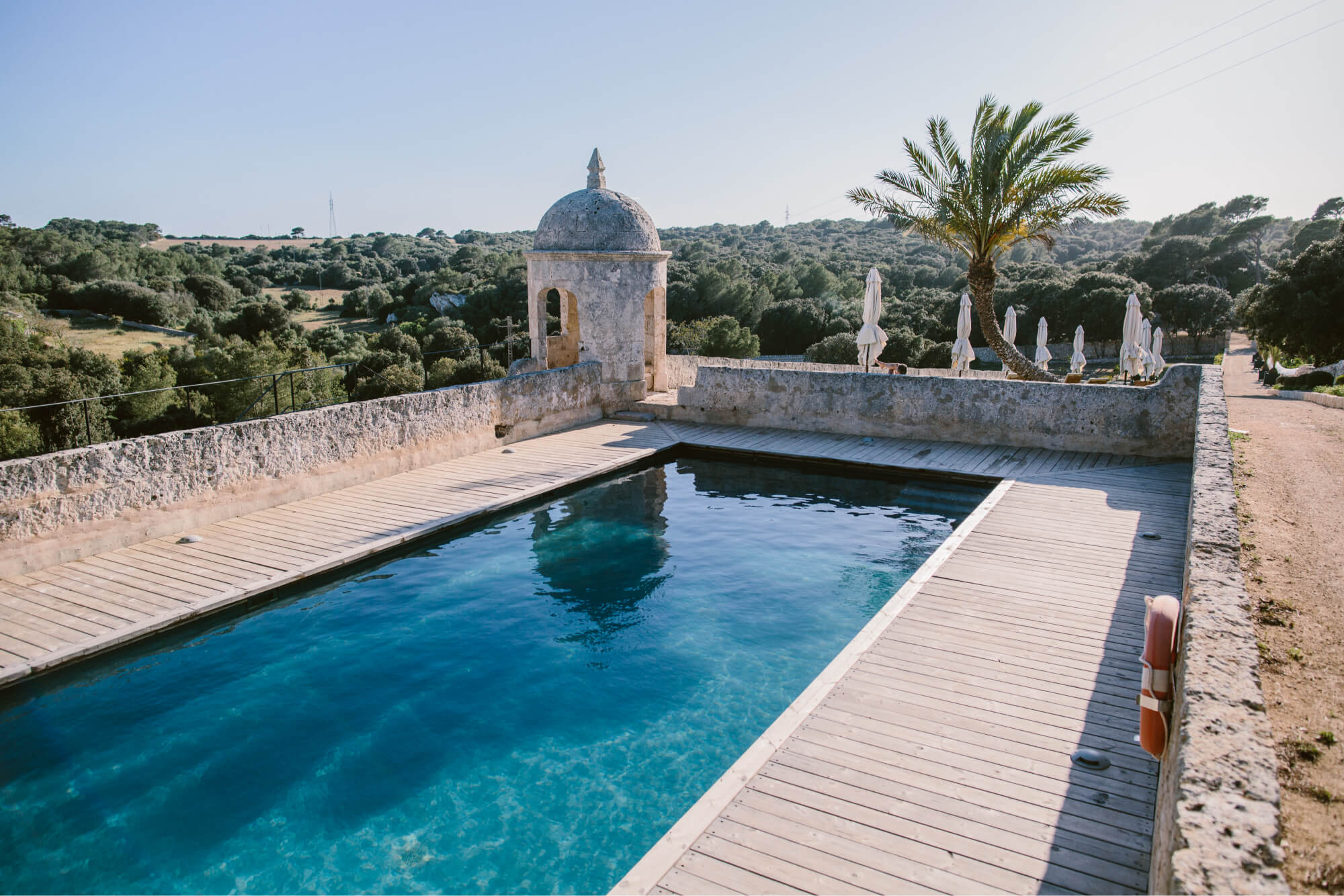 The outdoor pool at Santa Ponsa set among lush estate gardens, with a terrace and mature palm trees against the Menorcan sky