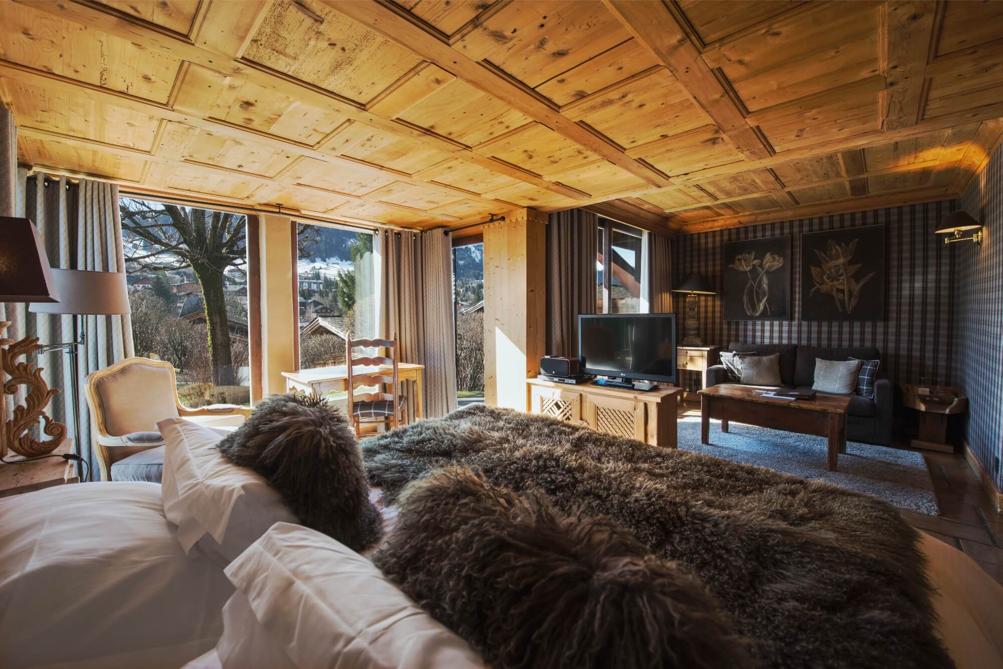 Interior of a wooden cabin featuring a bed with fluffy brown throw facing a television and sofa.